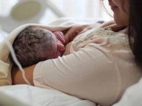 Uma mãe recém-parturiente, usando um roupão hospitalar, amamentando seu bebê recém-nascido.