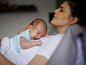 Uma mãe com aspecto de cansaço, deitada com um bebê chorando em seu colo. Uma mãe com aspecto de cansaço, deitada com um bebê chorando em seu colo.