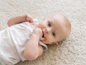 bebê deitado com uma das mãos na boca