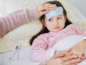 Criança doente deitada na cama com compressa na testa e termômetro ao lado