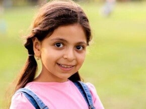 Menina usando macacão jeans e camiseta rosa sorrindo em um gramado verde Menina usando macacão jeans e camiseta rosa sorrindo em um gramado verde