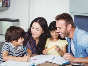 Uma família formada por pai, mãe, filho e filha sentados à mesa, sorrindo e interagindo.