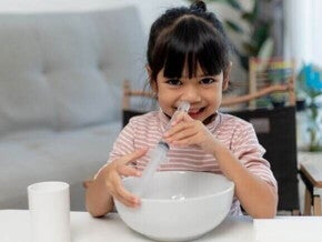 Um bebê deitado com a boca aberta, enquanto uma mão segura uma seringa próxima ao nariz do bebê