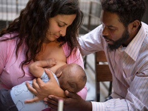 mãe amamentando um bebê enquanto um homem oferece suporte