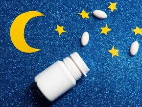 Frasco branco de comprimidos aberto com pílulas espalhadas sobre fundo azul com brilho, decorado com estrelas e uma lua amarela de papel.