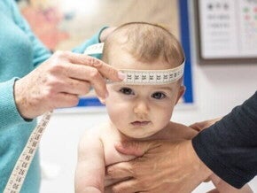 Bebê sendo examinado com uma fita métrica para medir o perímetro cefálico, acompanhamento médico essencial do crescimento infantil.