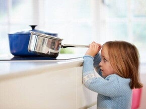 Uma criança em pé puxando o cabo de uma panela que está em cima do fogão.