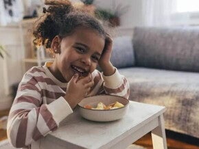 Foto de uma criança fazendo um lanche e comendo com as mãos uma vasilha de salada de frutas, um exemplo de alimento rico em vitamina C