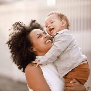 Mãe sorridente carrega o filho no colo, ilustrando a fase conhecida como terrible two. Mãe sorridente carrega o filho no colo, ilustrando a fase conhecida como terrible two.