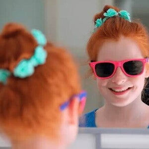 Menina sorri para a própria imagem no espelho. Se trata de uma criança de cerca de 9 anos usando óculos escuros com armação rosa. Menina sorri para a própria imagem no espelho. Se trata de uma criança de cerca de 9 anos usando óculos escuros com armação rosa.