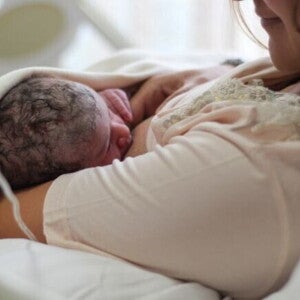Uma mãe recém-parturiente, usando um roupão hospitalar, amamentando seu bebê recém-nascido. Uma mãe recém-parturiente, usando um roupão hospitalar, amamentando seu bebê recém-nascido.
