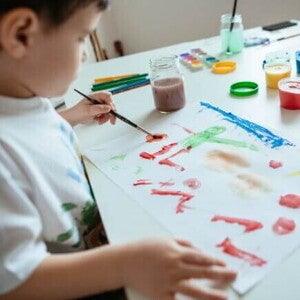 Criança canhota pintando uma folha branca com tinta e pincel Criança canhota pintando uma folha branca com tinta e pincel