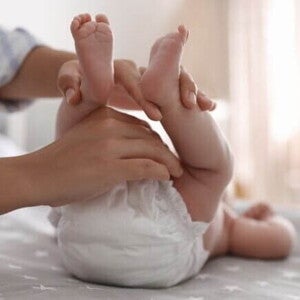 Uma pessoa segurando as pernas de um bebê deitado, preparando para fazer a troca da fralda.