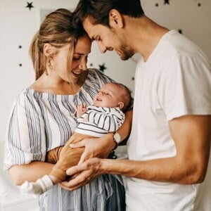 Um homem e uma mulher sorridentes seguram um bebê nos braços, dentro de um quarto infantil. Um homem e uma mulher sorridentes seguram um bebê nos braços, dentro de um quarto infantil.
