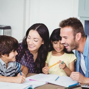 Uma família formada por pai, mãe, filho e filha sentados à mesa, sorrindo e interagindo. Uma família formada por pai, mãe, filho e filha sentados à mesa, sorrindo e interagindo.