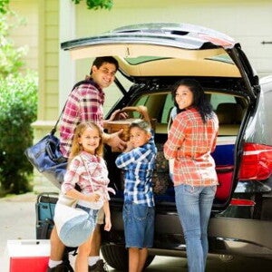 Família posando e sorrindo para a câmera, enquanto organiza malas dentro de um carro preto para sair de viagem Família posando e sorrindo para a câmera, enquanto organiza malas dentro de um carro preto para sair de viagem