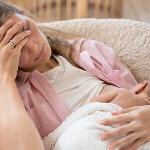 Imagem de uma mãe amamentando seu bebê com a mão na testa e semblante de cansada Imagem de uma mãe amamentando seu bebê com a mão na testa e semblante de cansada
