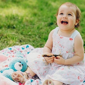 Menina de aproximadamente um ano usando vestido florido e sentada na grama de um parque. Menina de aproximadamente um ano usando vestido florido e sentada na grama de um parque.