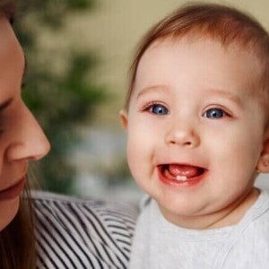 Nascimento dos dentes bebê Bebê sorrindo no colo da mãe, com os primeiros dentinhos visíveis, ilustrando o processo do nascimento dos dentes do bebê.
