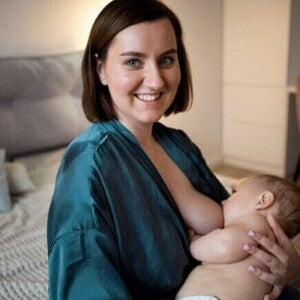 Uma mãe sorrindo, sentada, amamentando um bebê em seu colo Uma mãe sorrindo, sentada, amamentando um bebê em seu colo