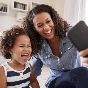 Sentadas no chão, mãe e filha sorriem ao tirar uma foto com o celular. As duas apresentam uma personalidade parecida. Sentadas no chão, mãe e filha sorriem ao tirar uma foto com o celular. As duas apresentam uma personalidade parecida.