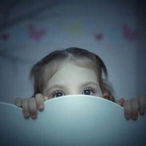 Sonambulismo infantil criança se esconde atrás de cabeceira de cama em quarto infantil, rosto com expressão assustada.