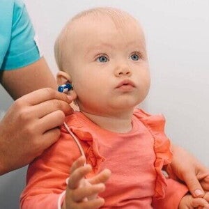 Teste da orelhinha Profissional da saúde aplicando o teste da orelhinha em um bebê no colo, usando um pequeno fone no ouvido da criança para verificar a capacidade auditiva.