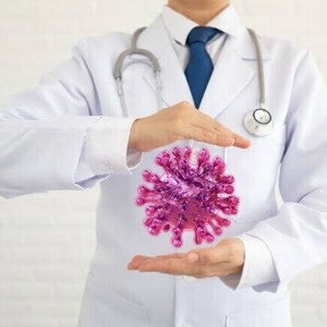 Um profissional da saúde em pé, com uma ilustração de um vírus colocada entre as suas mãos.