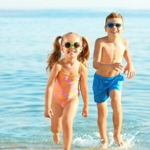 Duas crianças sorrindo e correndo na praia, usando óculos de sol e roupa de banho. Duas crianças sorrindo e correndo na praia, usando óculos de sol e roupa de banho.