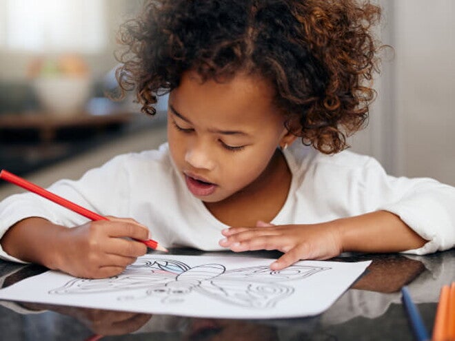 menina debruçada sobre mesa fazendo desenho