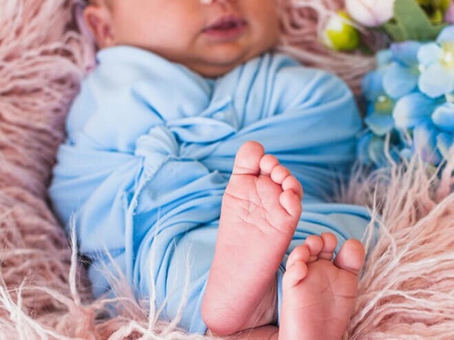 Ensaio fotográfico de bebê recém nascido deitado usando roupa azul claro.