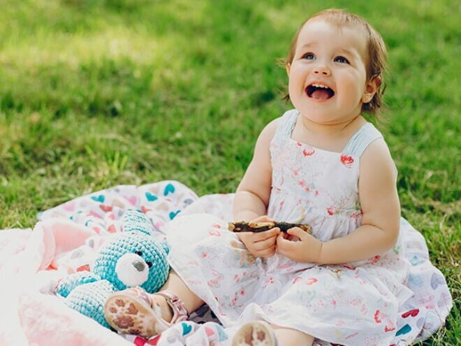 Menina de aproximadamente um ano usando vestido florido e sentada na grama de um parque. Menina de aproximadamente um ano usando vestido florido e sentada na grama de um parque.