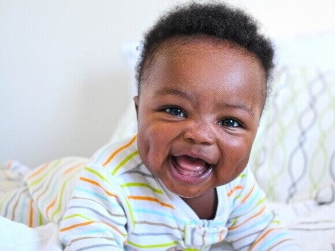 Bebê deitado e sorrindo, deitado em uma cama, sob um fundo branco. Bebê deitado e sorrindo, deitado em uma cama, sob um fundo branco.