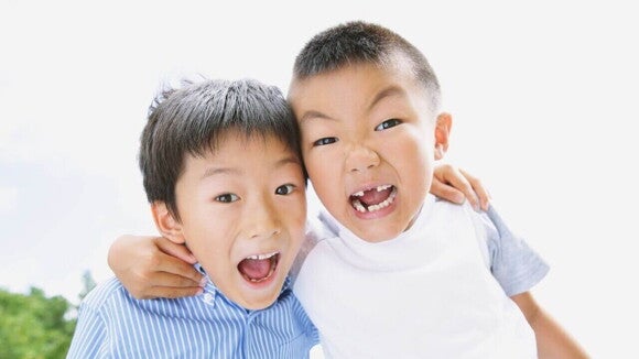 Dois meninos japoneses rindo e abraçados. Um deles, com um sorriso largo, exibe a ausência de alguns dentes, enquanto o outro sorri com a boca aberta.